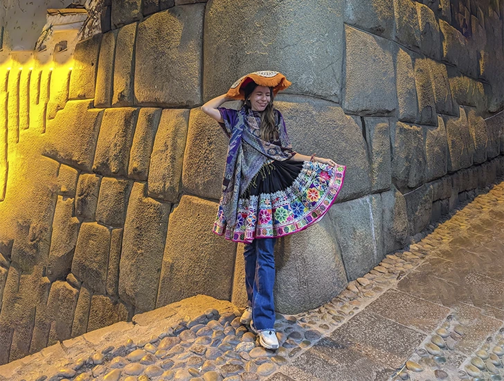 Mujer con traje tradicional andino en la calle Hatun Rumiyoc de Cusco, conocida por la piedra de los doce ángulos